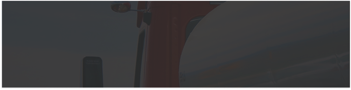 A close-up of a red truck, focusing on the cab and a shiny metallic tanker, with part of a side mirror and blurred background visible.