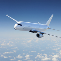 A white commercial airplane flies above the clouds in a clear blue sky, viewed from the front left side.
